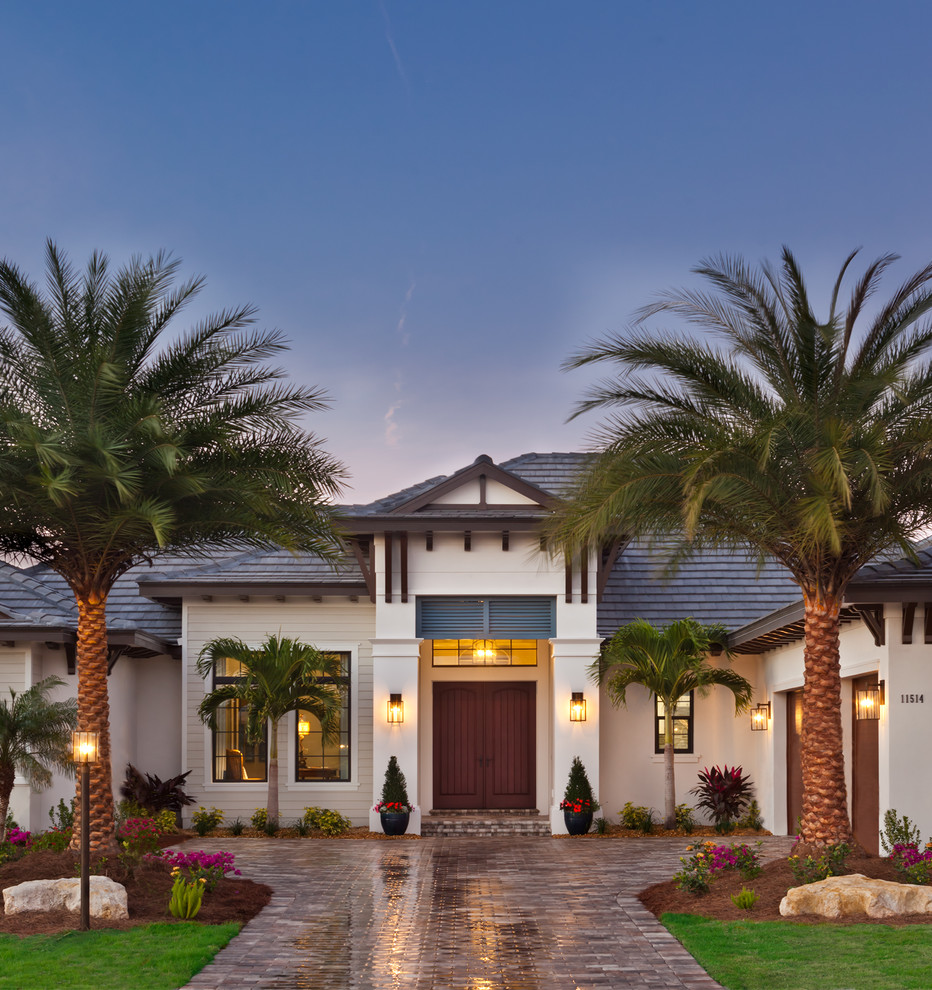 This is an example of an expansive beach style one-storey stucco beige house exterior in Tampa with a hip roof and a shingle roof.