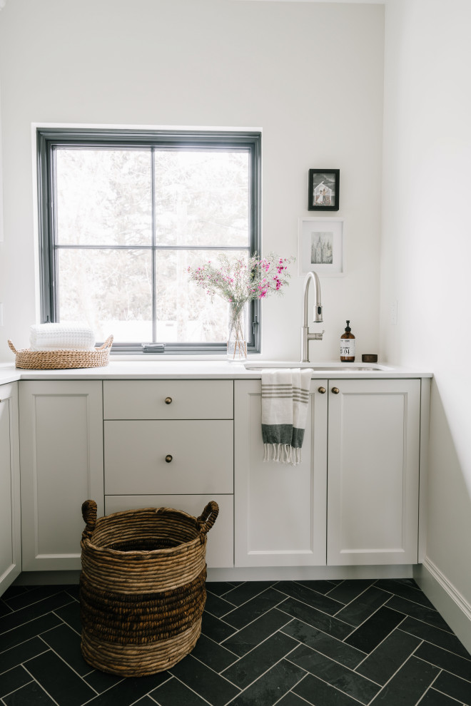 Medium sized traditional single-wall separated utility room in Salt Lake City with a built-in sink, shaker cabinets, white cabinets, engineered stone countertops, white walls, slate flooring, a side by side washer and dryer, black floors and white worktops.