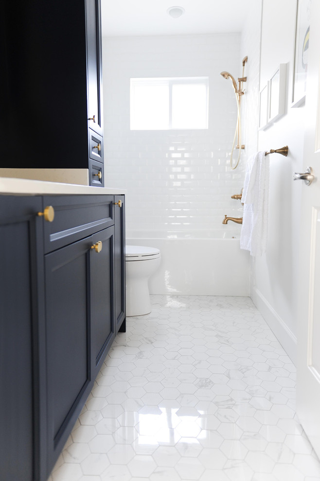 Photo of a transitional bathroom in Vancouver with shaker cabinets, blue cabinets, an alcove tub, a shower/bathtub combo, a two-piece toilet, white tile, subway tile, grey walls, ceramic floors, an undermount sink, engineered quartz benchtops, grey floor and an open shower.