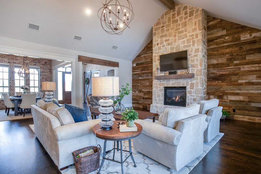 Photo of a large country open concept family room in Dallas with grey walls, dark hardwood floors, a standard fireplace, a stone fireplace surround, a wall-mounted tv and brown floor.