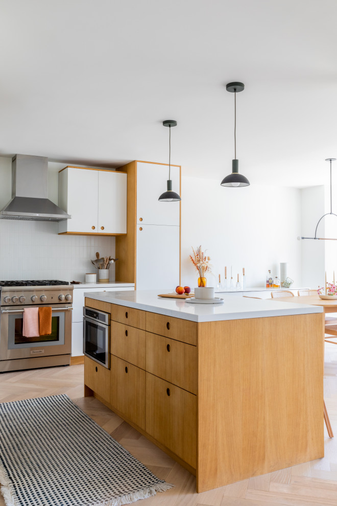 Example of a small danish l-shaped light wood floor and brown floor open concept kitchen design in San Francisco with an undermount sink, flat-panel cabinets, light wood cabinets, quartz countertops, white backsplash, ceramic backsplash, stainless steel appliances, an island and white countertops