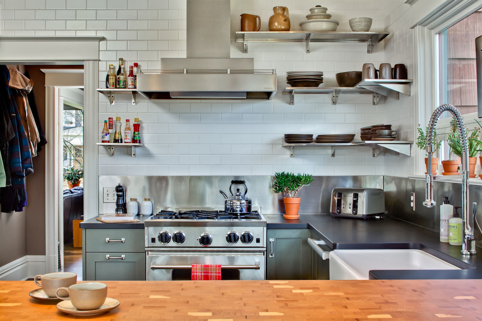This is an example of a transitional u-shaped kitchen in Seattle with a farmhouse sink, stainless steel appliances, green cabinets, white splashback and subway tile splashback.