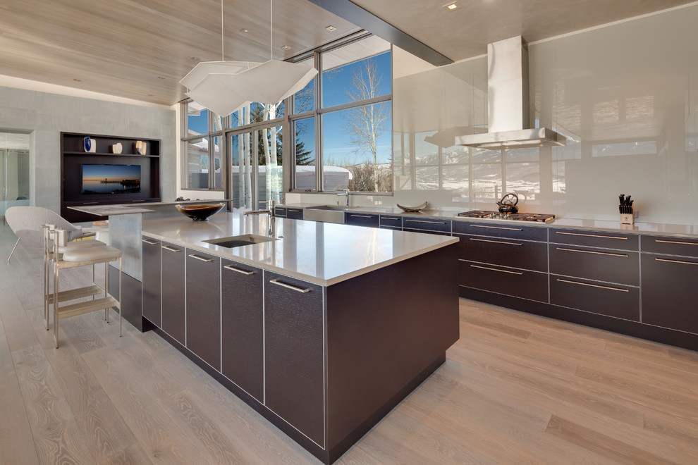 Large contemporary l-shaped eat-in kitchen in Denver with a farmhouse sink, flat-panel cabinets, dark wood cabinets, granite benchtops, beige splashback, stone slab splashback, panelled appliances, light hardwood floors and with island.