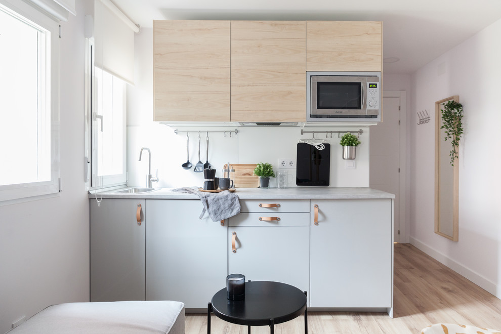 Photo of a small scandinavian single-wall open plan kitchen in Madrid with a drop-in sink, flat-panel cabinets, light wood cabinets, laminate benchtops, white splashback, window splashback, stainless steel appliances, laminate floors, no island, brown floor and grey benchtop.
