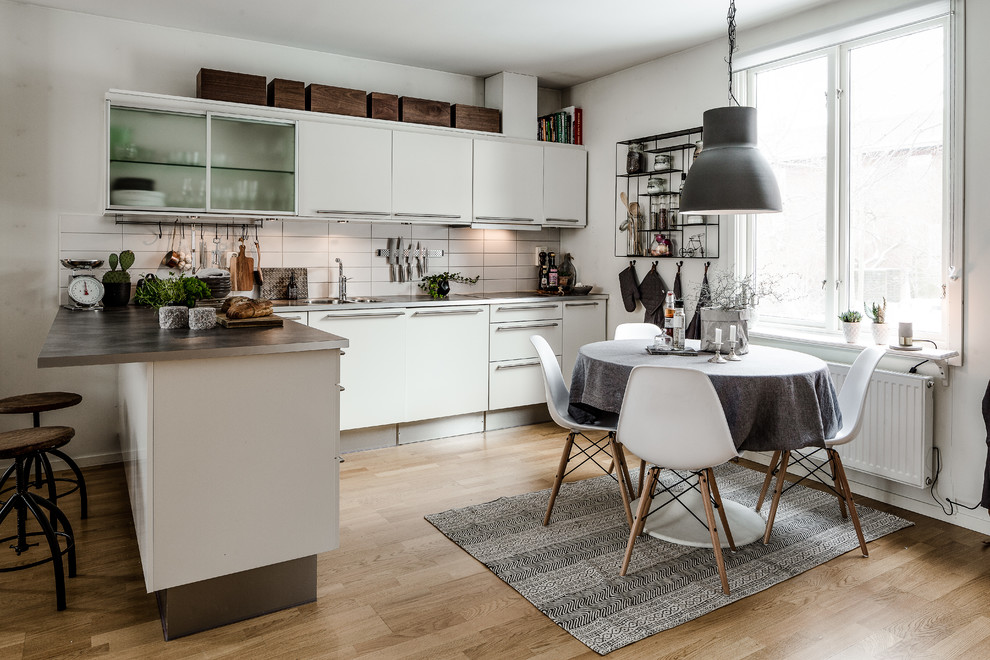 Inspiration for a mid-sized scandinavian l-shaped eat-in kitchen in Gothenburg with flat-panel cabinets, white cabinets, white splashback, medium hardwood floors, a peninsula, a double-bowl sink and wood benchtops.