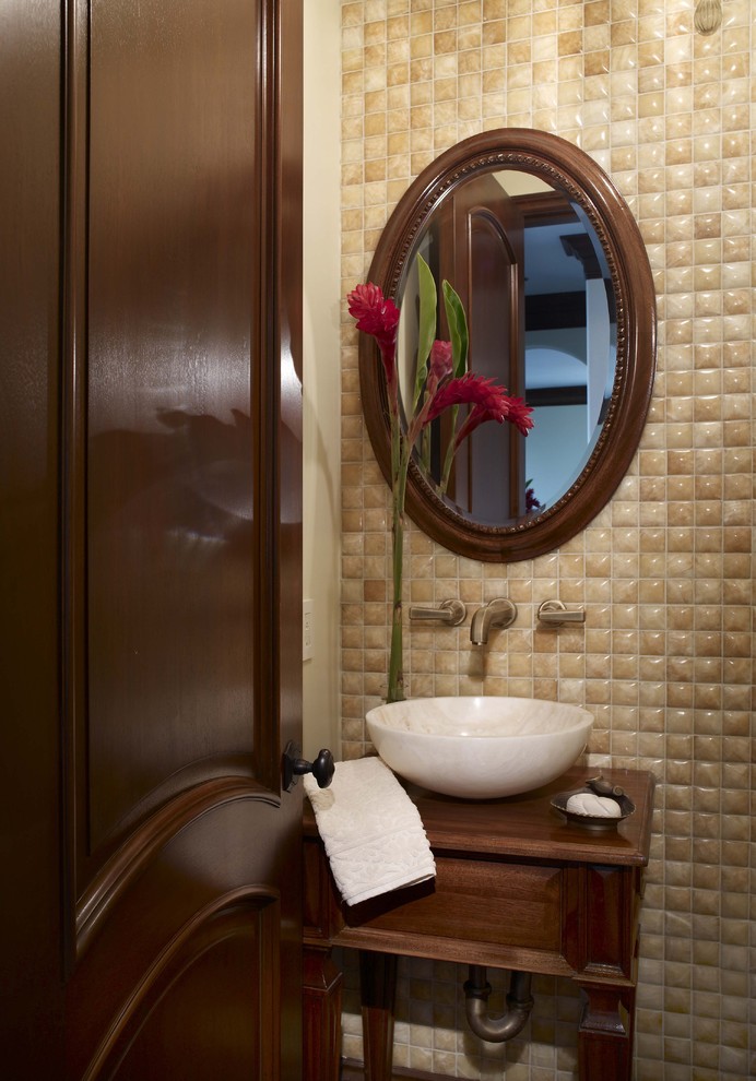 Inspiration for a small mediterranean powder room in Los Angeles with furniture-like cabinets, medium wood cabinets, beige tile, beige walls, a vessel sink and wood benchtops.