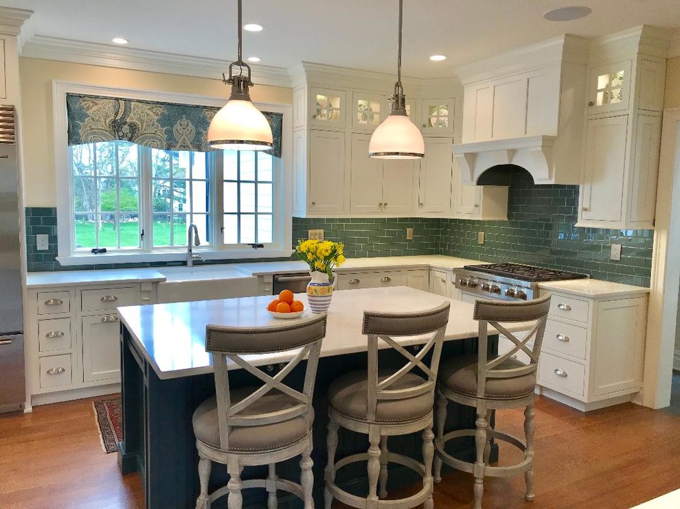 Large traditional l-shaped eat-in kitchen in New York with a farmhouse sink, beaded inset cabinets, white cabinets, quartz benchtops, green splashback, subway tile splashback, stainless steel appliances, light hardwood floors, with island, brown floor and white benchtop.