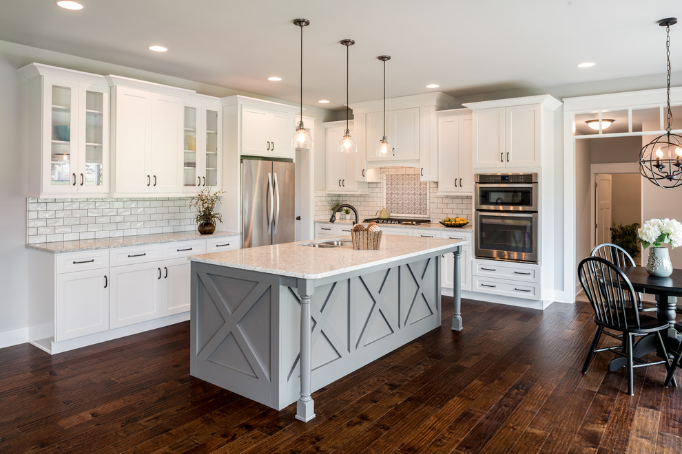 Design ideas for a country l-shaped eat-in kitchen in Philadelphia with a double-bowl sink, shaker cabinets, white cabinets, white splashback, subway tile splashback, stainless steel appliances, dark hardwood floors, with island and brown floor.