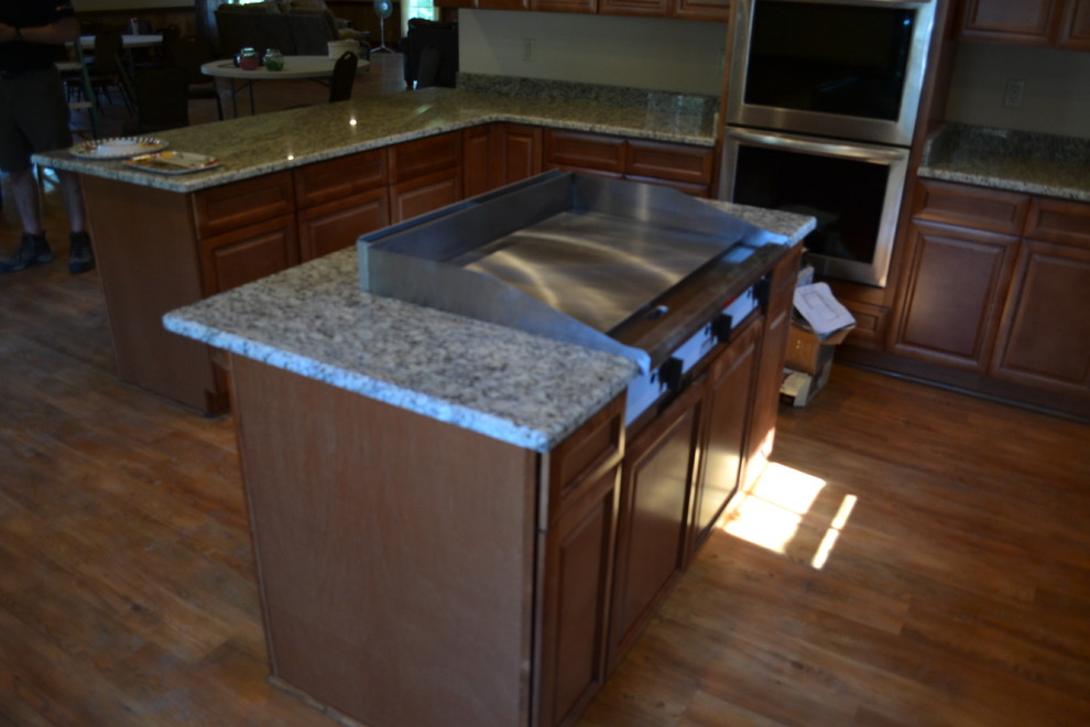 Kitchen - mid-sized rustic u-shaped medium tone wood floor kitchen idea in Atlanta with raised-panel cabinets, brown cabinets, granite countertops, stainless steel appliances and an island