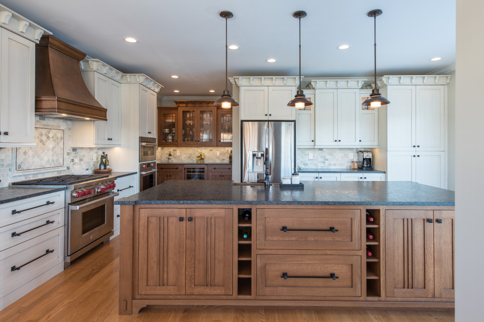 Photo of an expansive arts and crafts u-shaped kitchen in Other with a farmhouse sink, shaker cabinets, white cabinets, grey splashback, stainless steel appliances, medium hardwood floors, with island, brown floor and grey benchtop.
