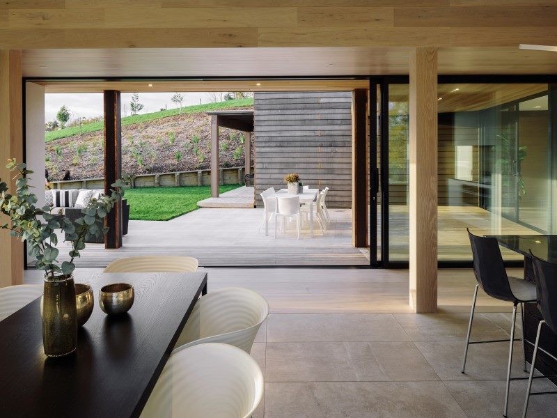 This is an example of a country open plan dining in Auckland with porcelain floors, a two-sided fireplace, a plaster fireplace surround and grey floor.