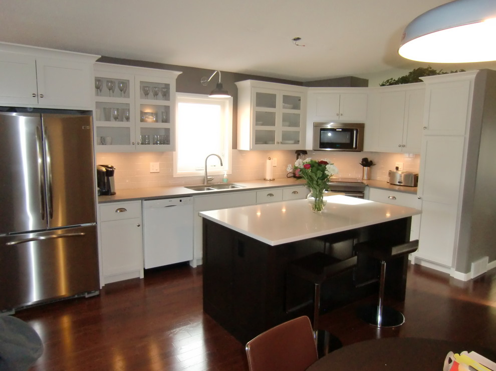 Mid-sized transitional l-shaped dark wood floor and brown floor eat-in kitchen photo with a double-bowl sink, shaker cabinets, white cabinets, quartz countertops, white backsplash, stainless steel appliances, an island and white countertops