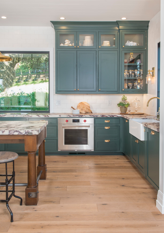 Design ideas for a large country galley eat-in kitchen in San Francisco with a drop-in sink, flat-panel cabinets, green cabinets, marble benchtops, white splashback, ceramic splashback, stainless steel appliances, medium hardwood floors, with island, brown floor and white benchtop.