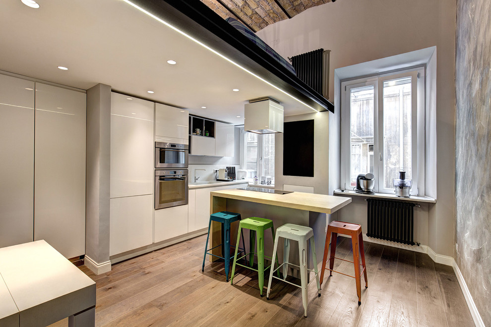 Photo of an industrial single-wall open plan kitchen in Rome with flat-panel cabinets, white cabinets, light hardwood floors and with island.