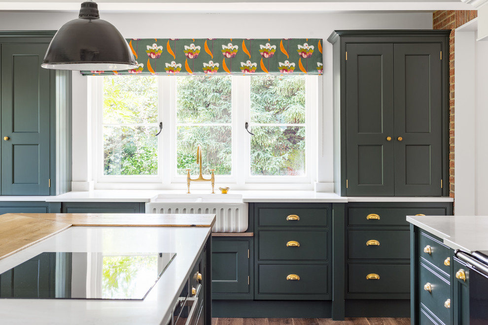 Photo of a large traditional u-shaped open plan kitchen in Manchester with a single-bowl sink, shaker cabinets, green cabinets, granite benchtops, white splashback, limestone splashback, black appliances, dark hardwood floors, with island, brown floor and white benchtop.
