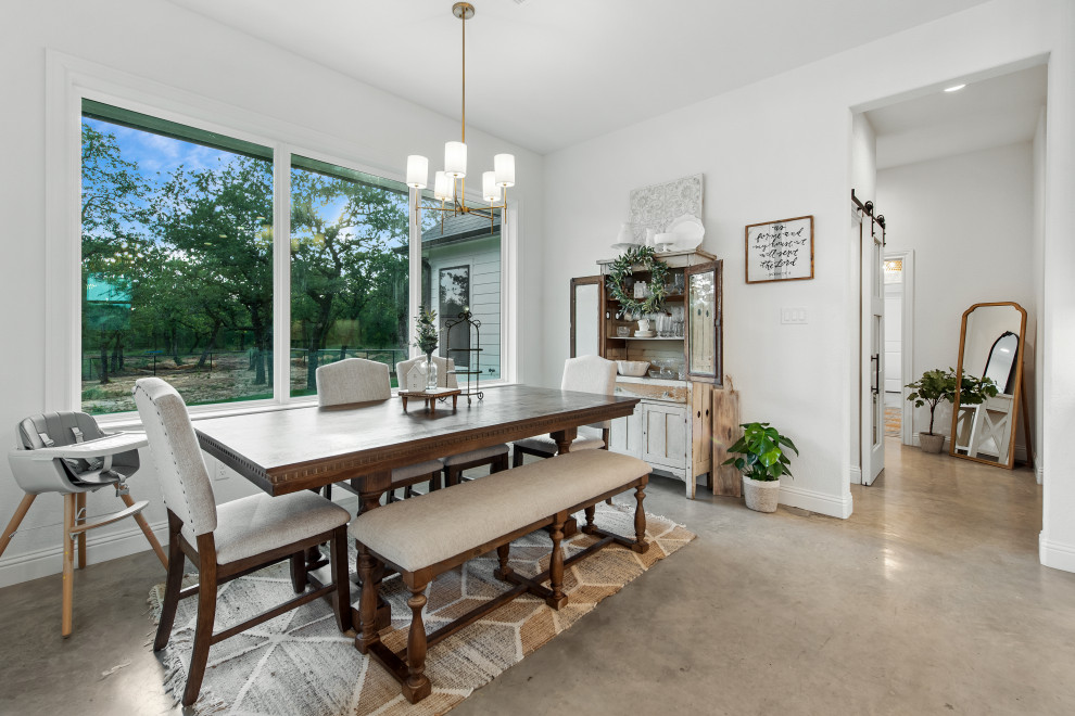 Foto di una sala da pranzo aperta verso la cucina country di medie dimensioni con pareti bianche, pavimento in cemento, pavimento beige e travi a vista