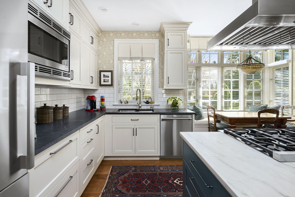 Enclosed kitchen - large transitional l-shaped medium tone wood floor and brown floor enclosed kitchen idea in Philadelphia with a double-bowl sink, recessed-panel cabinets, green cabinets, soapstone countertops, beige backsplash, ceramic backsplash, stainless steel appliances, an island and beige countertops