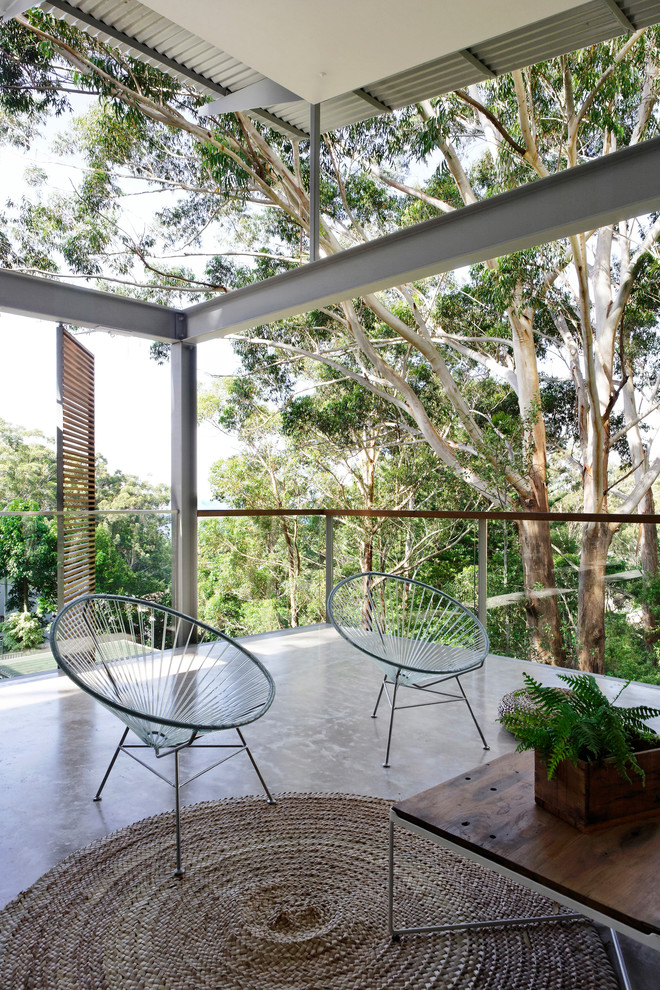 Large contemporary balcony in Sydney with a roof extension and glass railing.