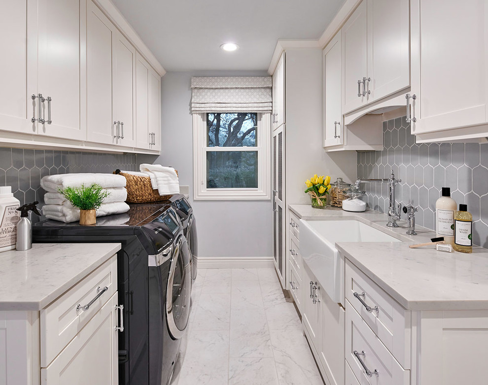 Photo of a mid-sized transitional galley dedicated laundry room in Other with a farmhouse sink, shaker cabinets, white cabinets, grey walls, porcelain floors, a side-by-side washer and dryer, white floor and white benchtop.