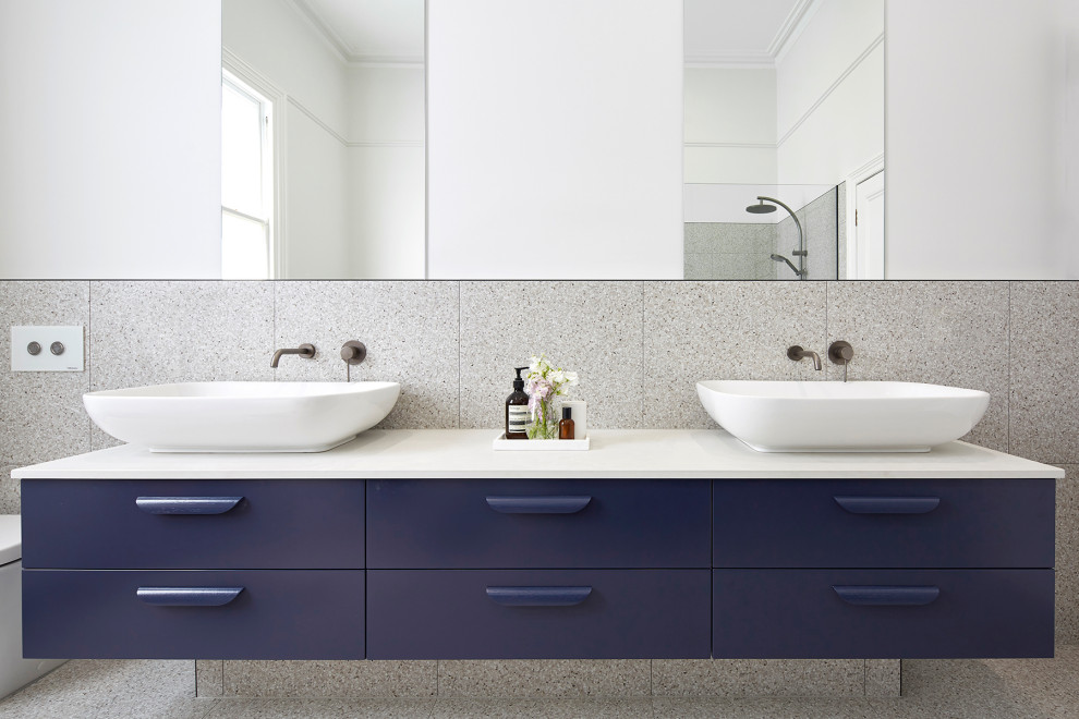 This is an example of a large modern kids bathroom in Melbourne with flat-panel cabinets, blue cabinets, a freestanding tub, an open shower, a wall-mount toilet, gray tile, multi-coloured walls, terrazzo floors, a vessel sink, engineered quartz benchtops, multi-coloured floor, an open shower and white benchtops.