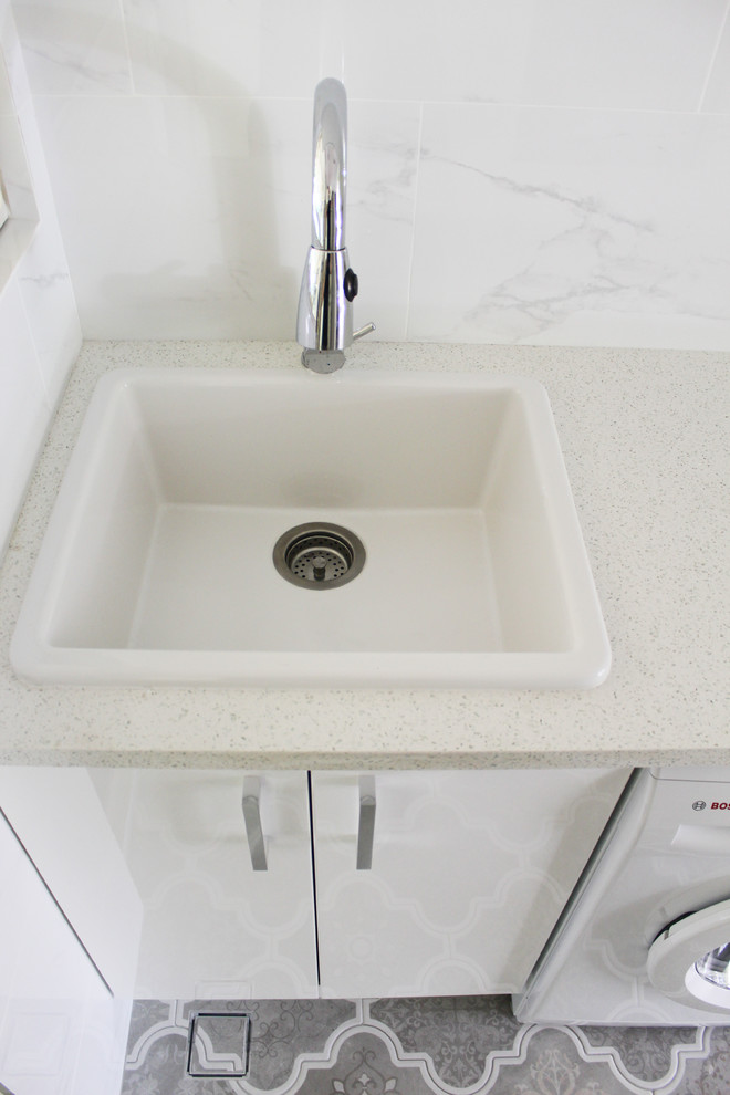 Photo of a small modern single-wall laundry room in Perth with a farmhouse sink, open cabinets, white cabinets, quartz benchtops, white walls, porcelain floors and multi-coloured floor.