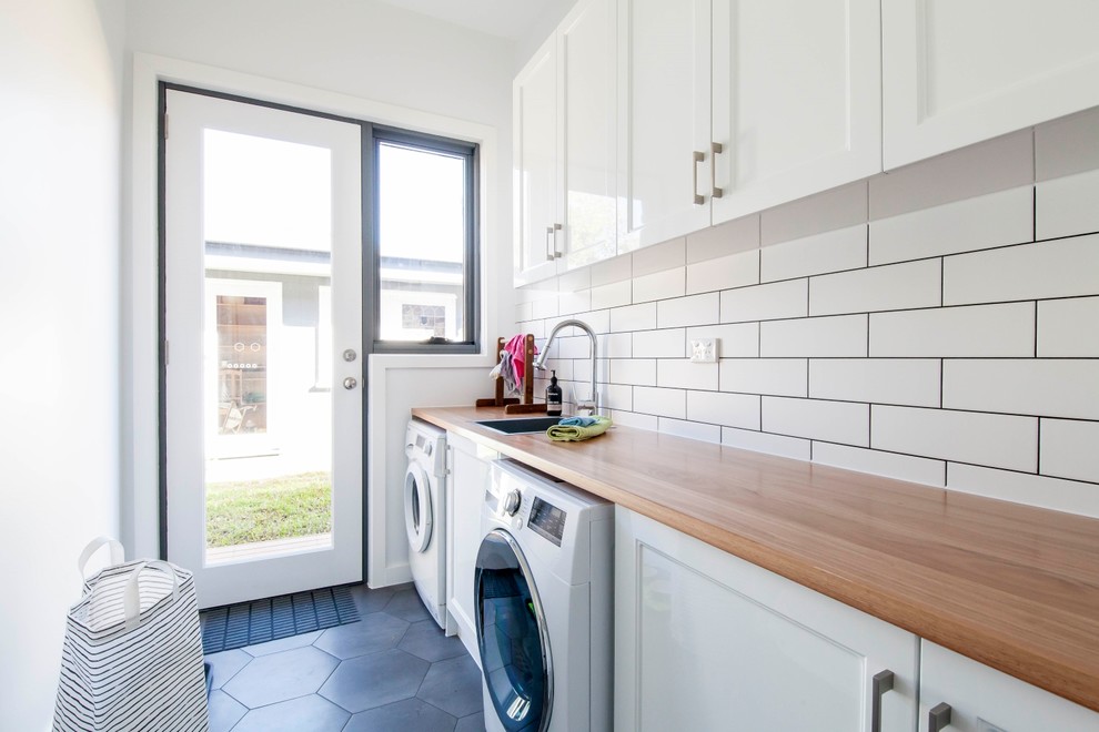Photo of a mid-sized transitional single-wall dedicated laundry room in Melbourne with white cabinets, wood benchtops, white walls, ceramic floors, grey floor, brown benchtop, a drop-in sink, recessed-panel cabinets and a side-by-side washer and dryer.