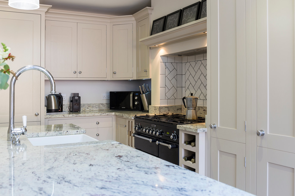 This is an example of a mid-sized traditional galley eat-in kitchen in London with a farmhouse sink, shaker cabinets, granite benchtops, black appliances, porcelain floors and with island.