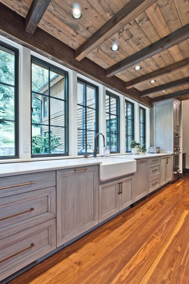 Inspiration for an expansive transitional u-shaped eat-in kitchen in Nashville with a farmhouse sink, recessed-panel cabinets, grey cabinets, quartz benchtops, stainless steel appliances, light hardwood floors, with island, brown floor and white benchtop.