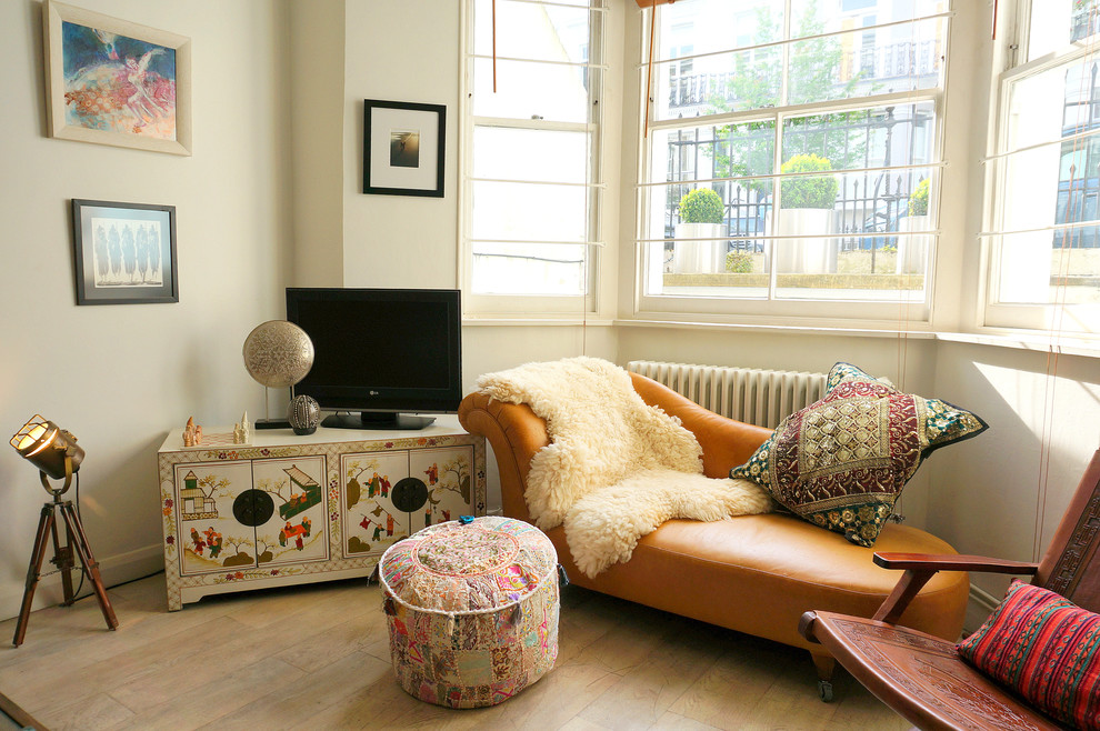 Eclectic living room in London with white walls, light hardwood floors and a freestanding tv.