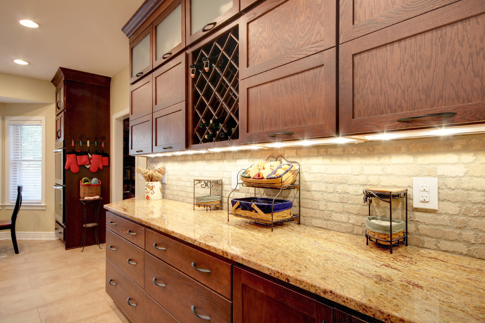 Example of a transitional eat-in kitchen design in Miami with an undermount sink, shaker cabinets, brown cabinets, granite countertops, beige backsplash, stone tile backsplash and stainless steel appliances