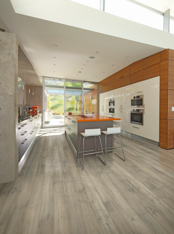 Inspiration for a large contemporary galley kitchen in Los Angeles with a drop-in sink, flat-panel cabinets, black cabinets, marble benchtops, stainless steel appliances, medium hardwood floors and orange benchtop.