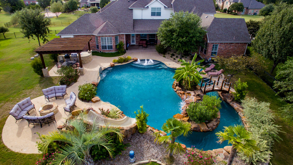 Photo of an expansive country backyard custom-shaped pool in Dallas with a water slide and stamped concrete.