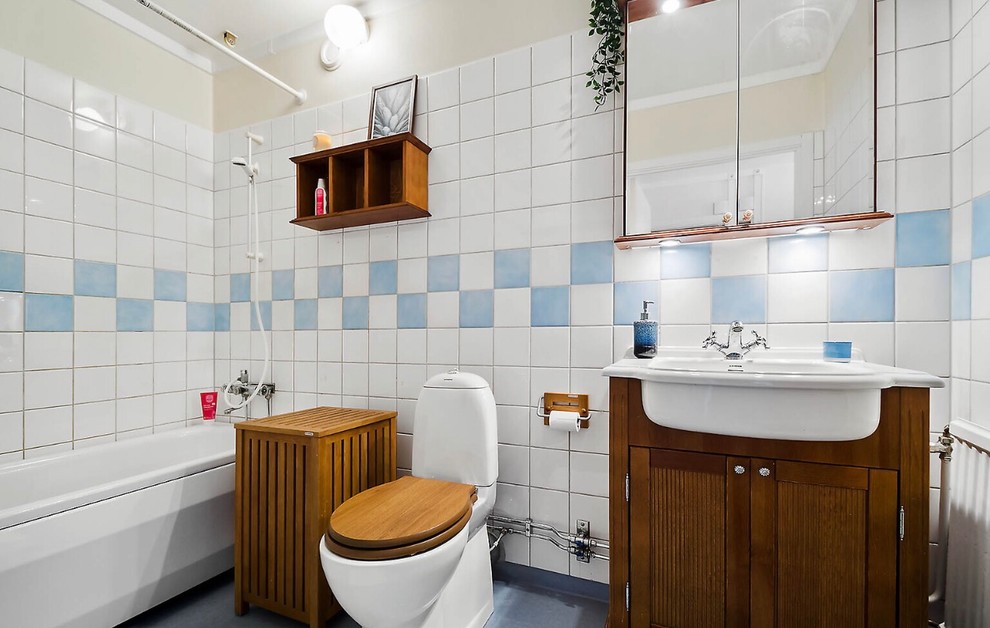 Photo of a scandinavian bathroom in Stockholm with recessed-panel cabinets, medium wood cabinets, a drop-in tub, a shower/bathtub combo, blue tile, white tile, beige walls, a drop-in sink, blue floor and a shower curtain.