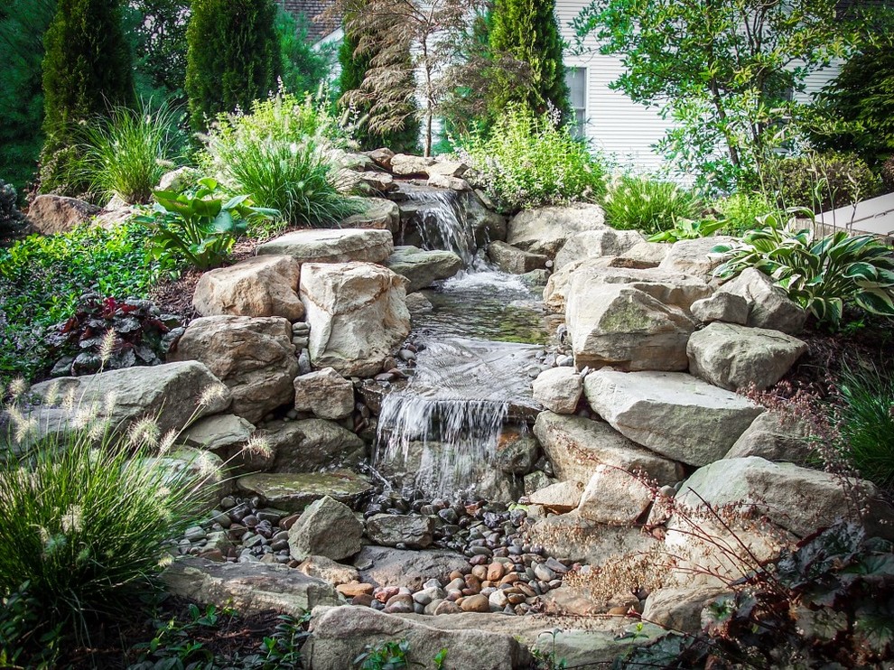 Photo of a mid-sized rustic partial sun backyard pond with a pergola.