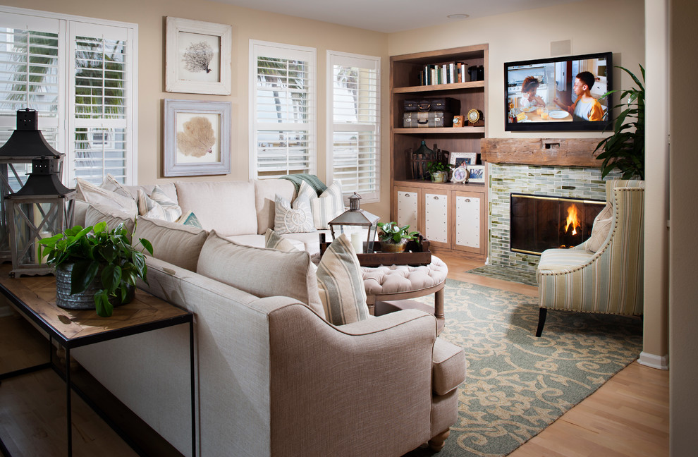 Photo of a mid-sized beach style open concept family room in San Diego with a tile fireplace surround, beige walls, light hardwood floors, a standard fireplace and a wall-mounted tv.