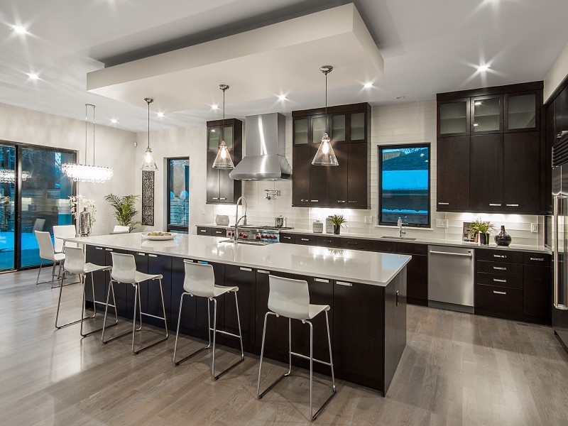 Photo of a contemporary single-wall open plan kitchen in Denver with a farmhouse sink, flat-panel cabinets, dark wood cabinets, white splashback, stainless steel appliances, with island and light hardwood floors.
