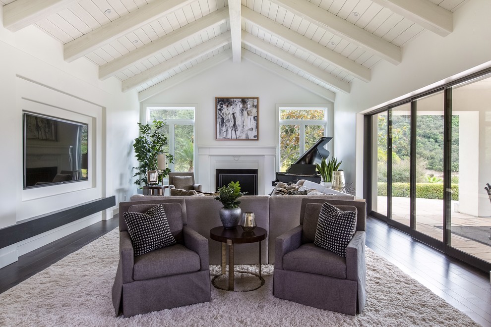 Large transitional open concept family room in San Diego with a music area, white walls, dark hardwood floors, a standard fireplace, a wood fireplace surround, a wall-mounted tv and brown floor.