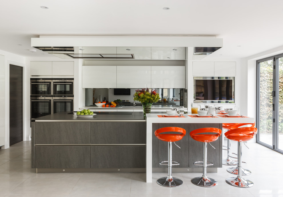 Large contemporary galley kitchen in London with an undermount sink, flat-panel cabinets, white cabinets, mirror splashback, stainless steel appliances, ceramic floors and with island.