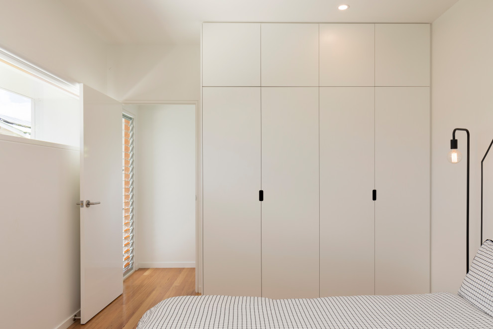 Cette image montre une armoire encastrée nordique avec des portes de placard blanches et un sol en bois brun.