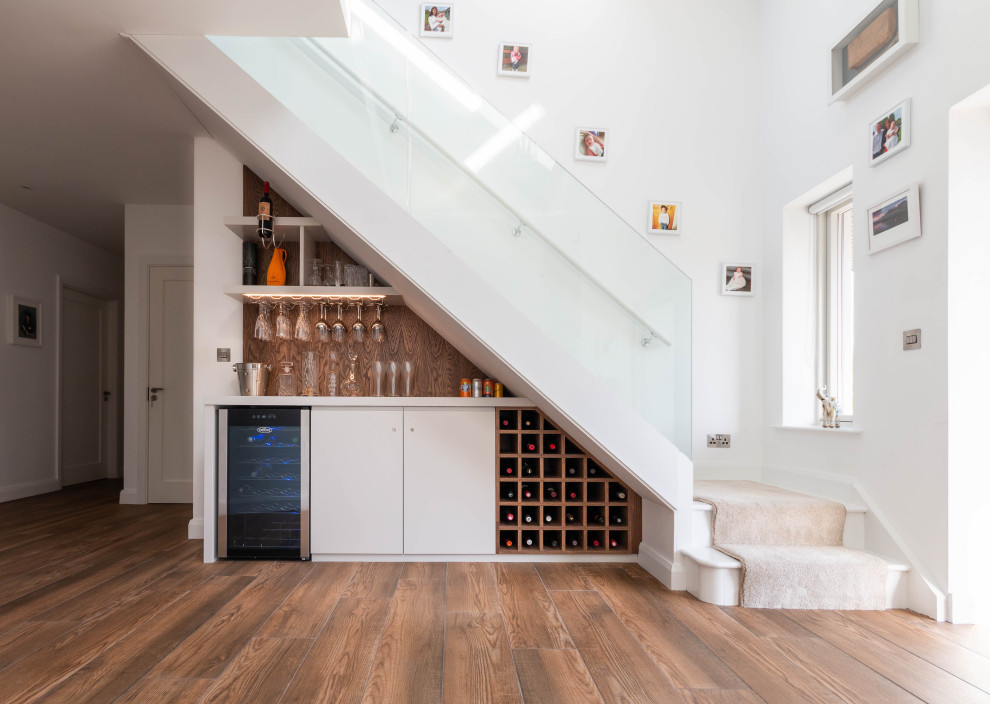 Mid-sized contemporary single-wall home bar in Other with flat-panel cabinets, white cabinets, brown splashback, medium hardwood floors, brown floor and white benchtop.