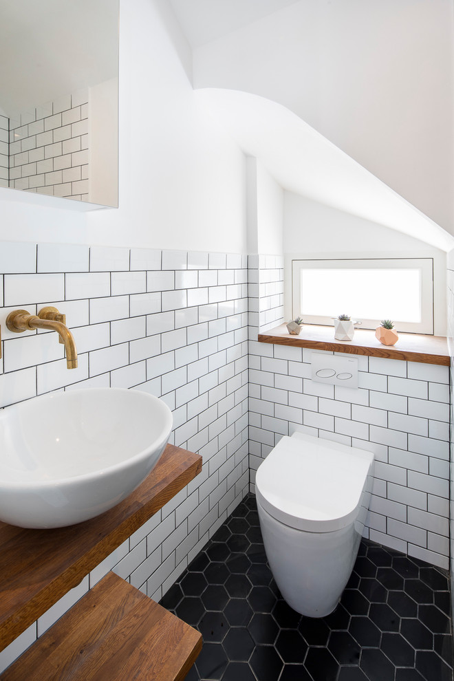 Design ideas for a small scandinavian powder room in London with white tile, subway tile, white walls, a vessel sink, wood benchtops, black floor, brown benchtops and a wall-mount toilet.