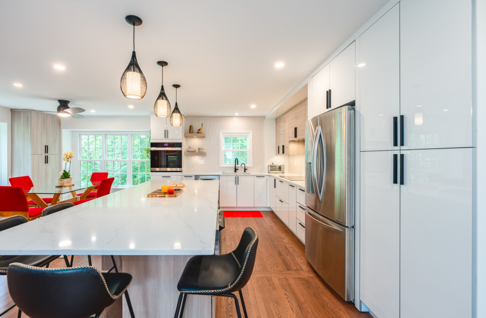 Mid-sized contemporary l-shaped eat-in kitchen in DC Metro with a single-bowl sink, flat-panel cabinets, white cabinets, quartzite benchtops, white splashback, porcelain splashback, stainless steel appliances, medium hardwood floors, with island and white benchtop.