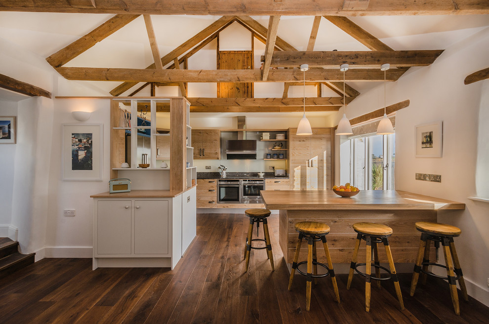 Photo of a mid-sized country eat-in kitchen in Cornwall with flat-panel cabinets, medium wood cabinets, wood benchtops, stainless steel appliances, medium hardwood floors and a peninsula.