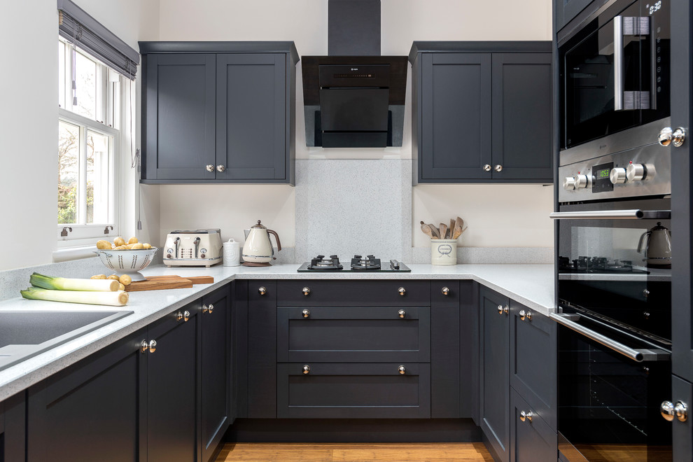 Inspiration for a mid-sized transitional u-shaped kitchen in Gloucestershire with granite benchtops, stone slab splashback, bamboo floors, no island, a drop-in sink, shaker cabinets, grey cabinets, grey splashback and black appliances.