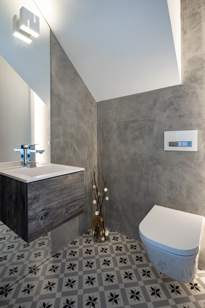 Inspiration for a large scandinavian powder room in Barcelona with flat-panel cabinets, cement tiles, multi-coloured floor, dark wood cabinets, a wall-mount toilet, grey walls, an integrated sink and white benchtops.