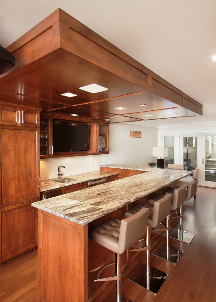 Inspiration for a large arts and crafts u-shaped seated home bar in Vancouver with a drop-in sink, recessed-panel cabinets, medium wood cabinets, quartzite benchtops, white splashback and medium hardwood floors.