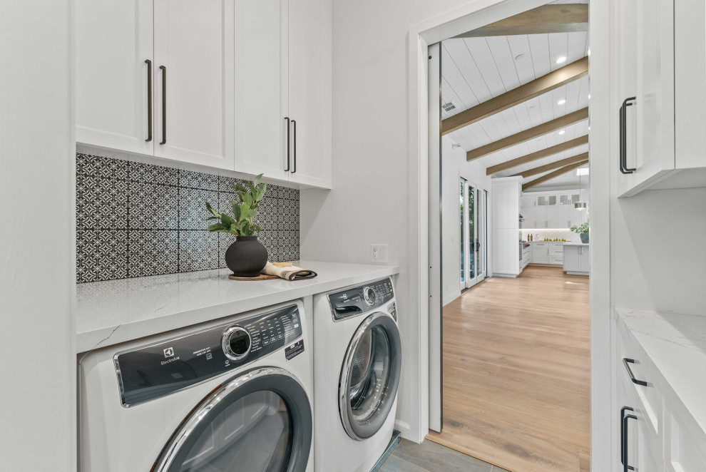 Photo of an expansive modern galley utility room in San Francisco with an undermount sink, recessed-panel cabinets, white cabinets, quartzite benchtops, multi-coloured splashback, mosaic tile splashback, multi-coloured walls, slate floors, a side-by-side washer and dryer, grey floor and white benchtop.