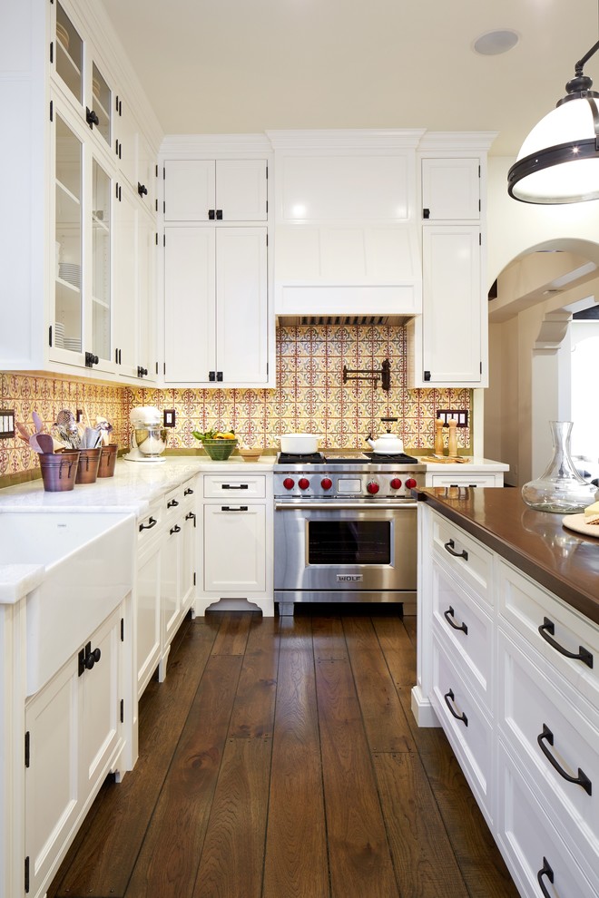 Inspiration for a mid-sized traditional l-shaped eat-in kitchen in Los Angeles with a farmhouse sink, glass-front cabinets, white cabinets, limestone benchtops, yellow splashback, mosaic tile splashback, black appliances, medium hardwood floors, with island and brown floor.