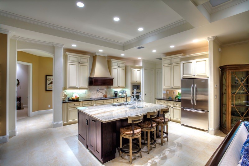 This is an example of a large tropical l-shaped eat-in kitchen in Miami with beige cabinets, beige splashback, stainless steel appliances, with island, a double-bowl sink and white floor.
