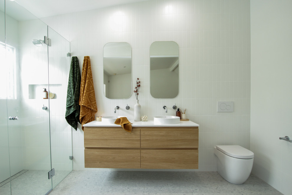 Photo of a mid-sized contemporary 3/4 bathroom in Sydney with medium wood cabinets, a one-piece toilet, white tile, white walls, a vessel sink, grey floor, a hinged shower door, white benchtops, a niche, a double vanity and a floating vanity.